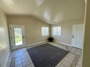 Foyer featuring a textured ceiling, plenty of natural light, light tile patterned floors, and lofted ceiling