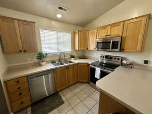 Kitchen with light tile patterned flooring, a sink, stainless steel appliances, vaulted ceiling, and visible vents