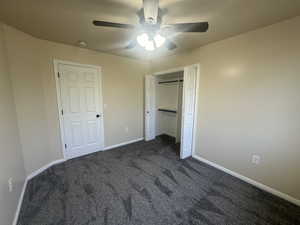 Unfurnished bedroom with baseboards, ceiling fan, a closet, and dark carpet
