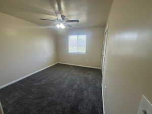 Spare room with dark colored carpet, a ceiling fan, baseboards, and a textured ceiling
