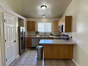 Kitchen with appliances with stainless steel finishes, a sink, a textured ceiling, a peninsula, and visible vents