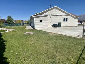 Rear view of property featuring fence, a patio, central AC unit, a lawn, and an outdoor fire pit