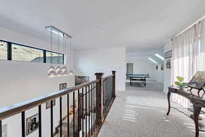 Upstairs hallway featuring carpet flooring, an upstairs landing, plenty of natural light, and vaulted ceiling