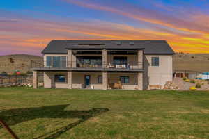 Back of property with stucco siding, a yard, stone siding, and fence