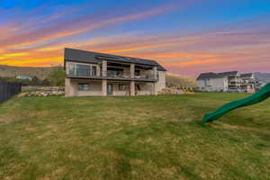 Back of house at dusk featuring a yard and fence