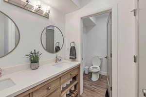 Bathroom with double vanity, a sink, wood finished floors, and toilet