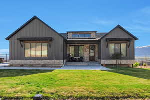 Rear view of house with a shingled roof, board and batten siding, a yard, and stone siding