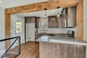 Kitchen featuring dark brown cabinetry, a sink, light stone counters, a peninsula, and stainless steel appliances