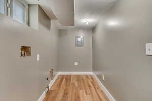 Clothes washing area featuring washer hookup, electric panel, laundry area, baseboards, and light wood-style floors