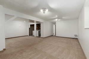 Finished basement featuring baseboards, a textured ceiling, and light carpet