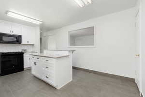 Kitchen featuring light stone countertops, baseboards, white cabinets, backsplash, and black appliances