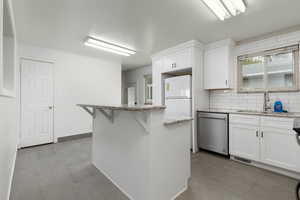 Kitchen featuring visible vents, a center island, stainless steel dishwasher, a sink, and white cabinetry