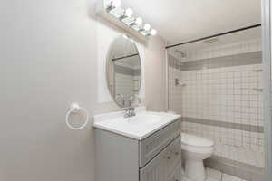 Full bathroom with vanity, a textured ceiling, tiled shower, and visible vents