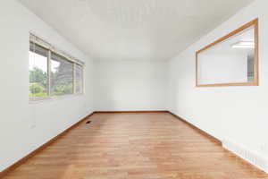 Unfurnished room featuring baseboards, light wood finished floors, a textured ceiling, and visible vents
