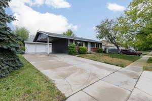 Ranch-style house featuring an attached garage, driveway, a carport, and a front lawn