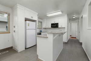 Kitchen with backsplash, visible vents, black microwave, white cabinets, and freestanding refrigerator