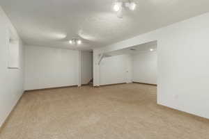 Finished below grade area with baseboards, a textured ceiling, and light colored carpet