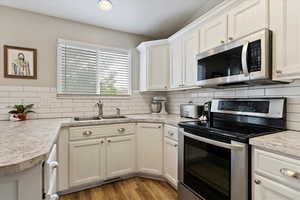 Kitchen featuring light wood-style flooring, a sink, stainless steel appliances, light countertops, and decorative backsplash