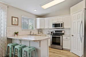 Kitchen featuring a peninsula, a sink, white cabinetry, appliances with stainless steel finishes, and tasteful backsplash