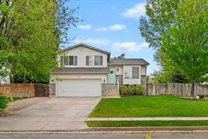 Split level home featuring an attached garage, driveway, fence, and a front yard