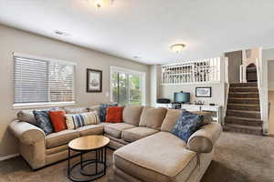 Carpeted living room featuring built in desk, a textured ceiling, stairway, and visible vents