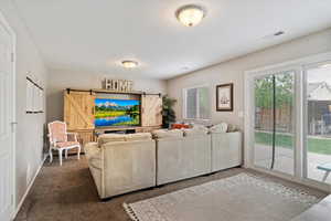 Carpeted living room featuring a barn door, baseboards, and visible vents