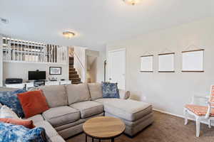 Living room featuring carpet, visible vents, baseboards, and stairs