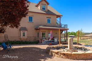 Back of property featuring stucco siding, fence, a balcony, and an outdoor fire pit