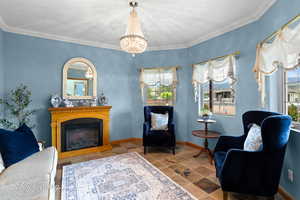 Sitting room with an inviting chandelier, a glass covered fireplace, stone tile floors, baseboards, and ornamental molding