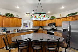 Kitchen featuring brown cabinets, a sink, a kitchen breakfast bar, stainless steel appliances, and visible vents