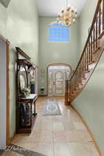 Entrance foyer featuring stairs, a high ceiling, a chandelier, and baseboards