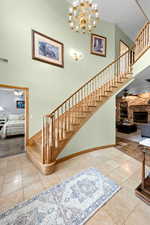 Stairs with a high ceiling, ceiling fan with notable chandelier, a stone fireplace, and visible vents
