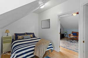 Apartment Bedroom with a textured ceiling, baseboards, wood finished floors, and lofted ceiling