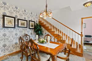 Dining area featuring baseboards, a chandelier, stairway, and wallpapered walls