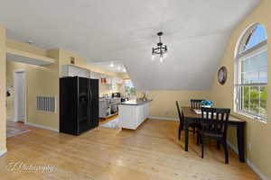 Apartment Kitchen featuring black fridge with ice dispenser, light wood-type flooring, white cabinetry, and visible vents