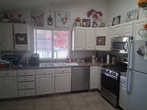 Kitchen featuring a sink, light tile patterned floors, stainless steel appliances, and white cabinetry