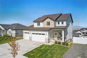Traditional-style house featuring covered porch, a front yard, fence, concrete driveway, and stone siding