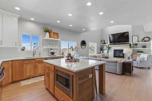 Kitchen with a glass covered fireplace, light wood-type flooring, light countertops, stainless steel microwave, and a sink