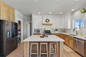Kitchen with a sink, light wood finished floors, appliances with stainless steel finishes, and light countertops