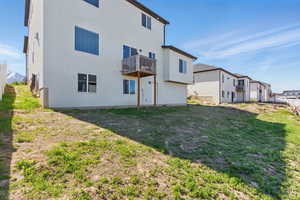 Rear view of property featuring stucco siding, a yard, and a balcony