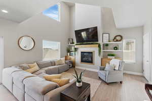 Living room featuring a glass covered fireplace, recessed lighting, baseboards, light wood-type flooring, and a towering ceiling