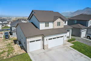 View of front facade featuring a shingled roof, stone siding, board and batten siding, cooling unit, and driveway
