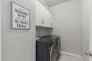Clothes washing area with separate washer and dryer, tile patterned flooring, cabinet space, and baseboards