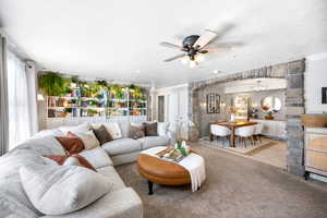 Carpeted living room featuring crown molding, tile patterned floors, and ceiling fan with notable chandelier