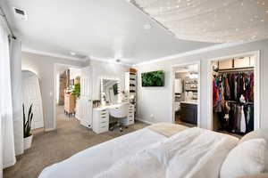 Carpeted bedroom with visible vents, crown molding, baseboards, a spacious closet, and ensuite bathroom
