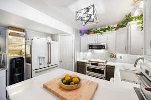 Kitchen with an inviting chandelier, decorative backsplash, light countertops, white cabinets, and premium appliances