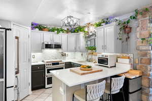 Kitchen with an inviting chandelier, a peninsula, white appliances, light countertops, and backsplash