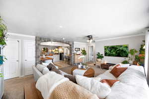 Living room with arched walkways, ornamental molding, light carpet, and a ceiling fan