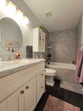 Bathroom featuring visible vents, wood finished floors, vanity, toilet, and tiled shower / bath combo