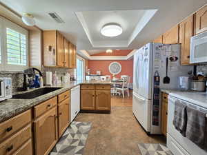 Kitchen featuring visible vents, a sink, a peninsula, a tray ceiling, and white appliances